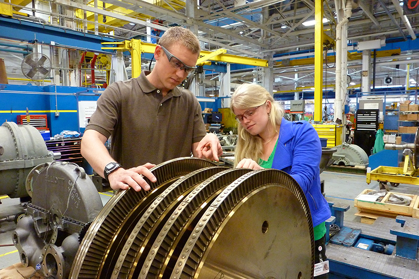 Two employees wearing safety goggles look at equipment in a service center.
